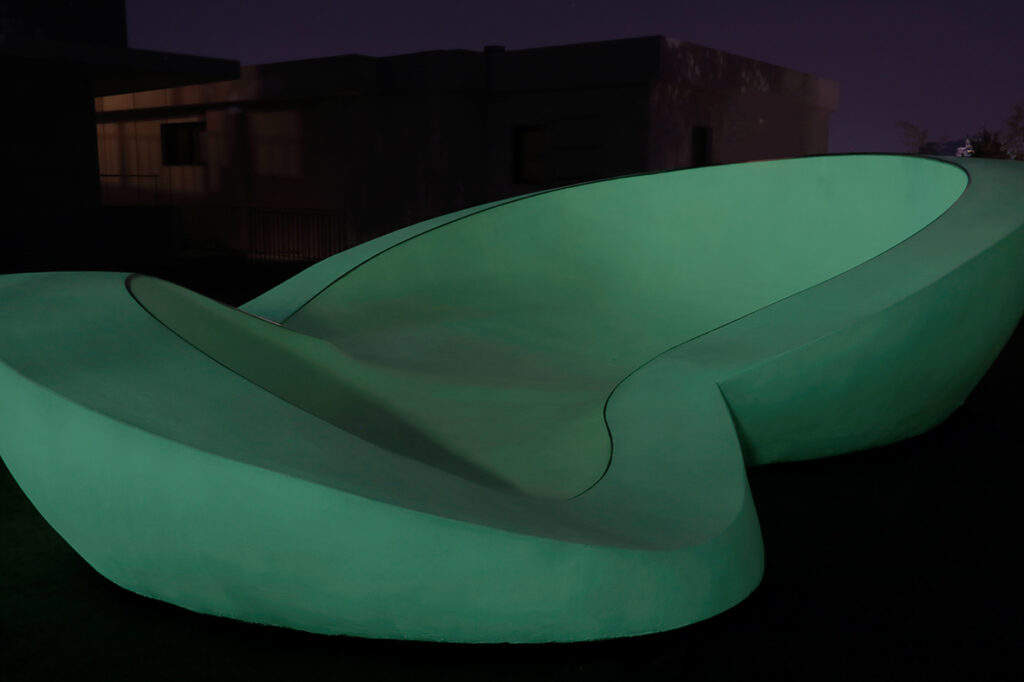 An organically shaped large skate ramp faintly glows in a dark night image.