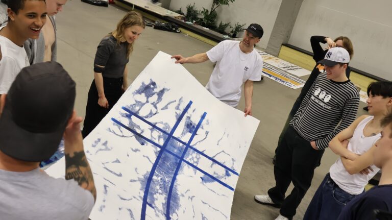 Studenter vid Bryggeriets gymnasium samlade kring ett verk skapat av skateboards med färg under hjulen som åkt över en stor canvas.
