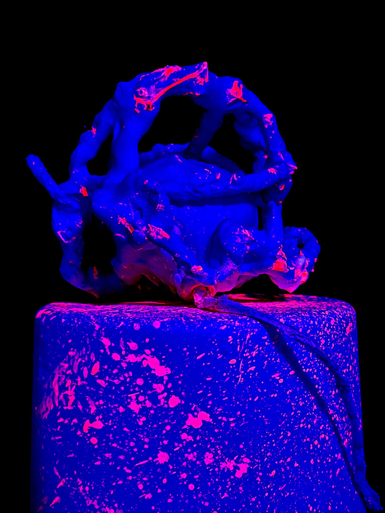 Luminous sculpture in blue and pink in an entirely black room.