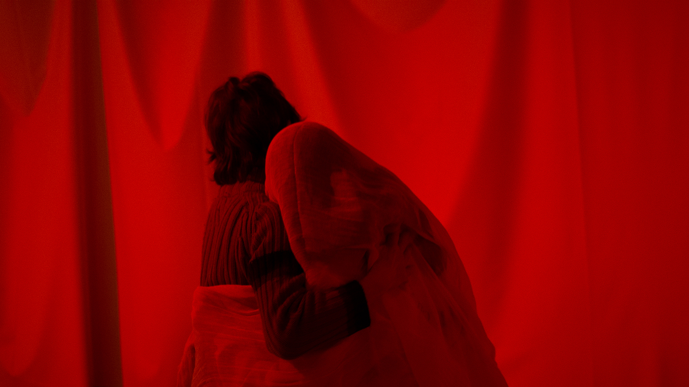 A person and a figure embrace each other in a completely red room.