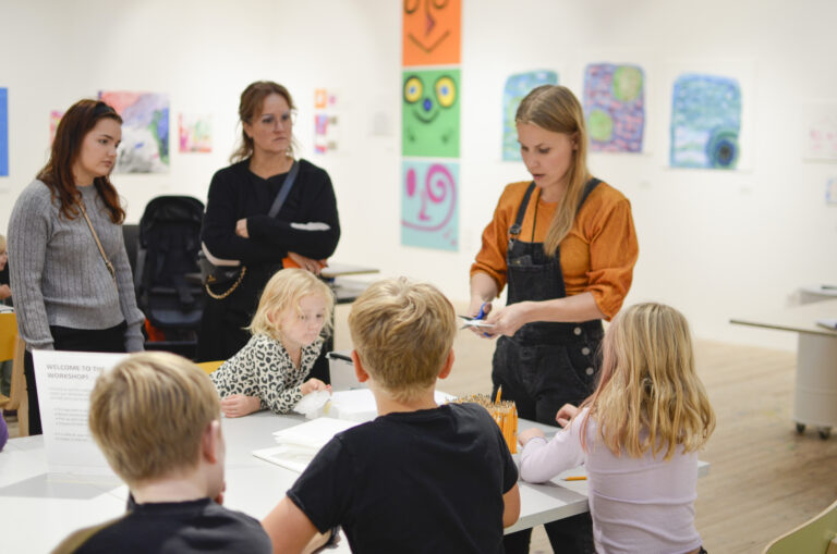 En grupp personer står samlade runt en kvinnlig pedagog som demonstrerar workshopen som ska äga rum.