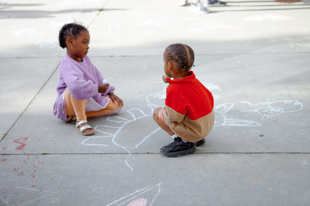 Två barn sitter på marken som har fina teckningar ritade med utomhuskritor.
