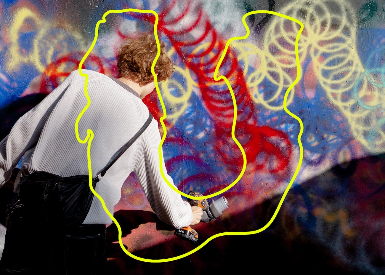 Person som målar med sprayfärg på vägg med gula, röda och blå färger