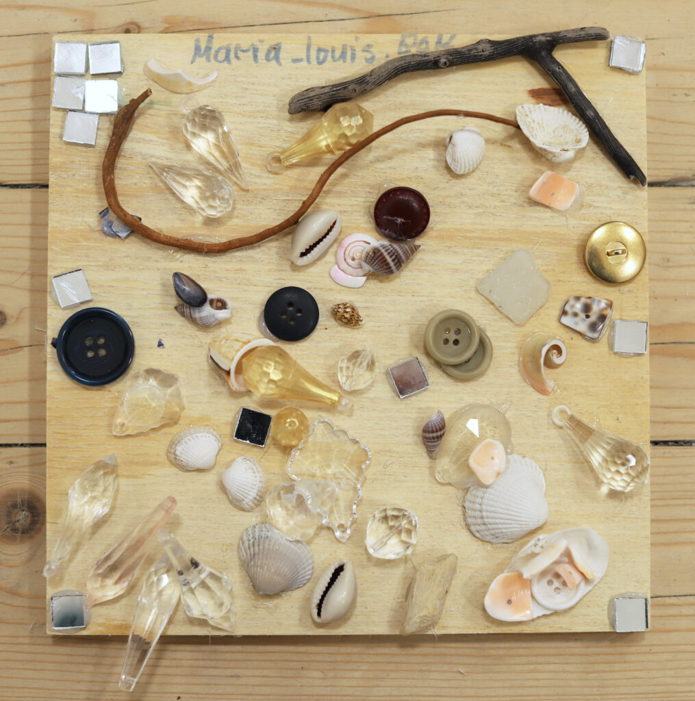 A wooden board decorated with buttons, seashells, and other small natural-colored items.