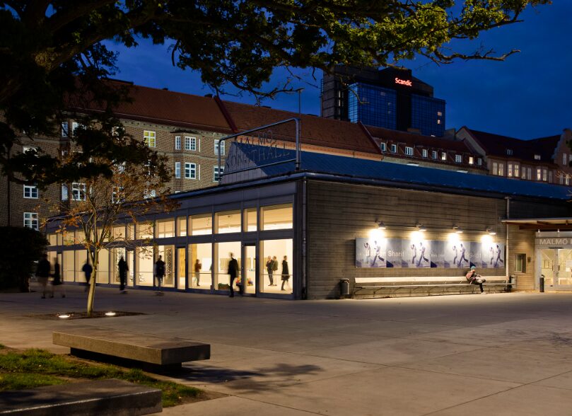 Malmö Konsthall in evening light, photographed from the outside. Inside, you can see about ten people walking around