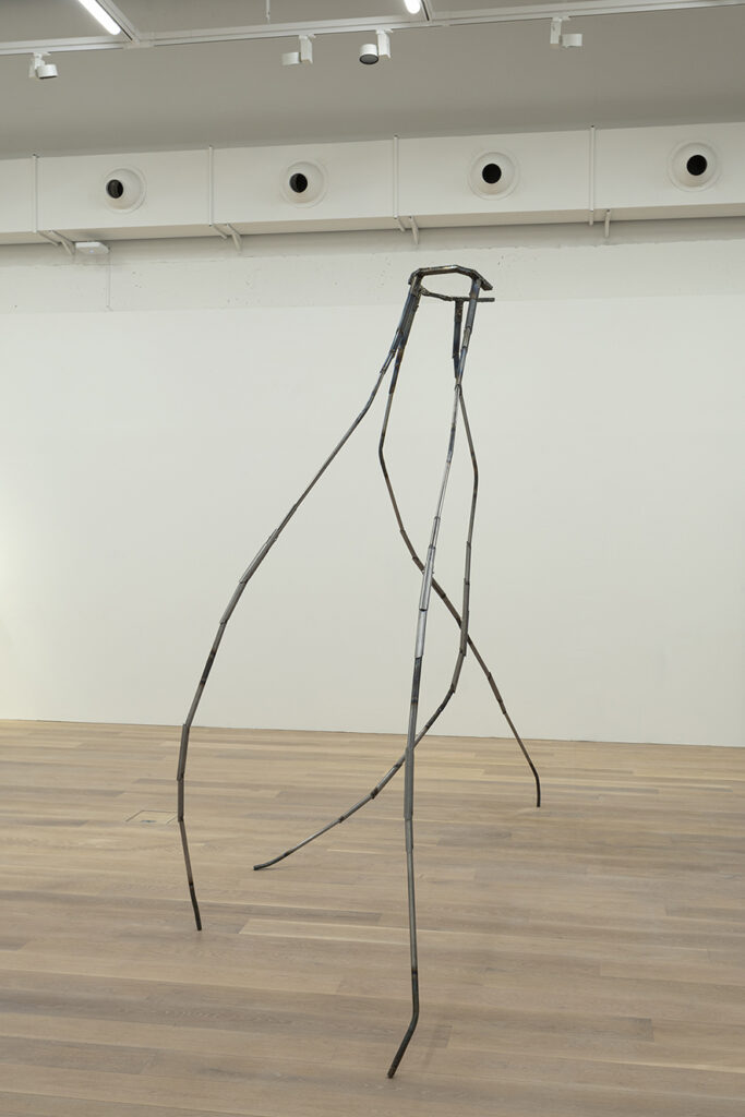 An artwork by Hanni Kamaly – a spider-like metal structure stands on four tall and slender legs.