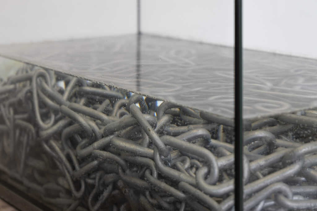 An artwork by Ina Nian – heavy metal chains placed in an aquarium filled with water.