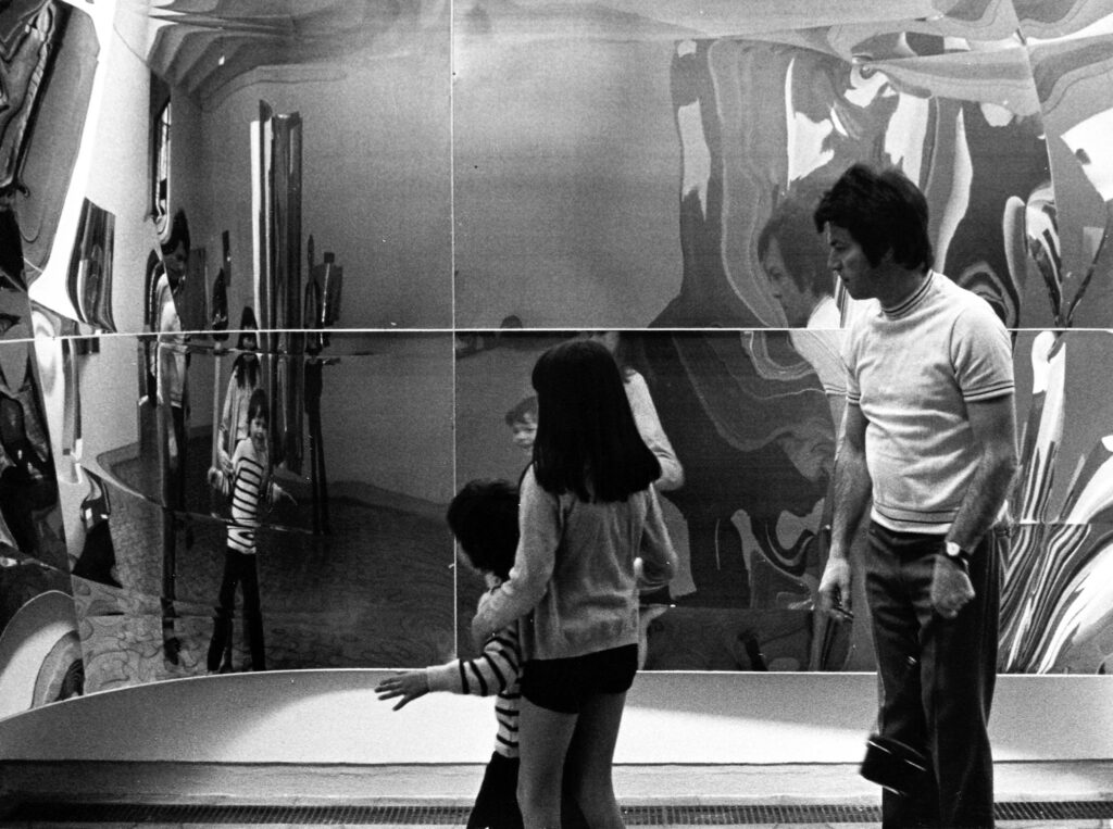 A man and a girl stand in front of one of Lars Fredrikson's works, a mirror that distorts reflections and reproduces images of the viewer. The photo is in black and white and was taken in 1972.