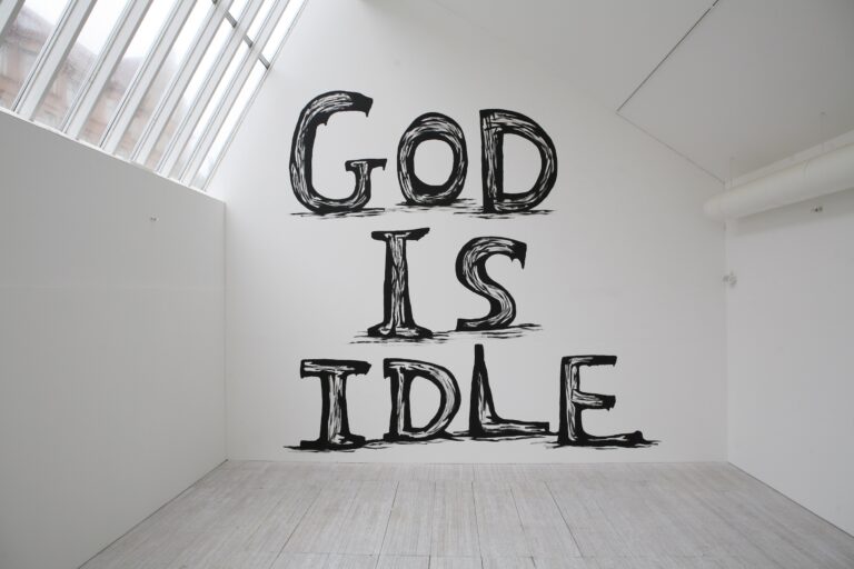 En stor väggmålning med texten "God is Idle" i svart handskriven text