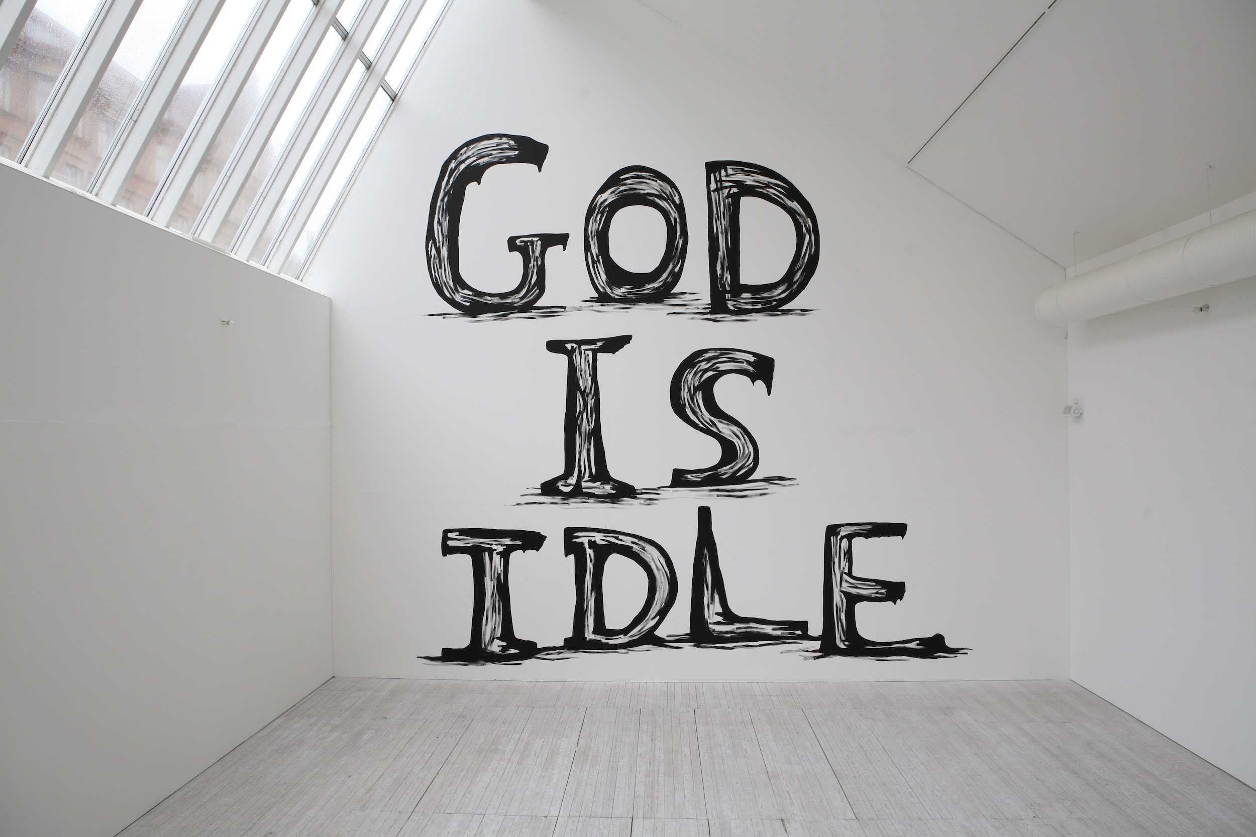 En stor väggmålning med texten "God is Idle" i svart handskriven text