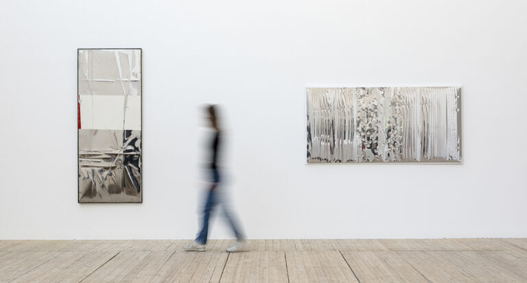 Installationsvy med två bearbetade metallspeglar och en person i rörelse i Malmö Konsthall.