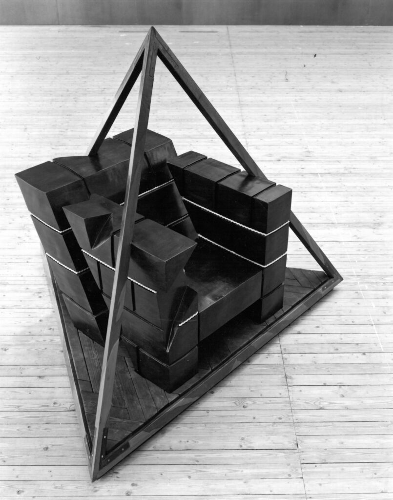 A chair made of cubes inside a triangle construction of steel.