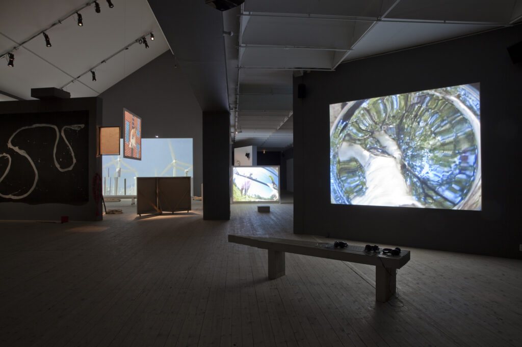 Flera väggar där video projiceras på i ett mörkt konsthallsrum