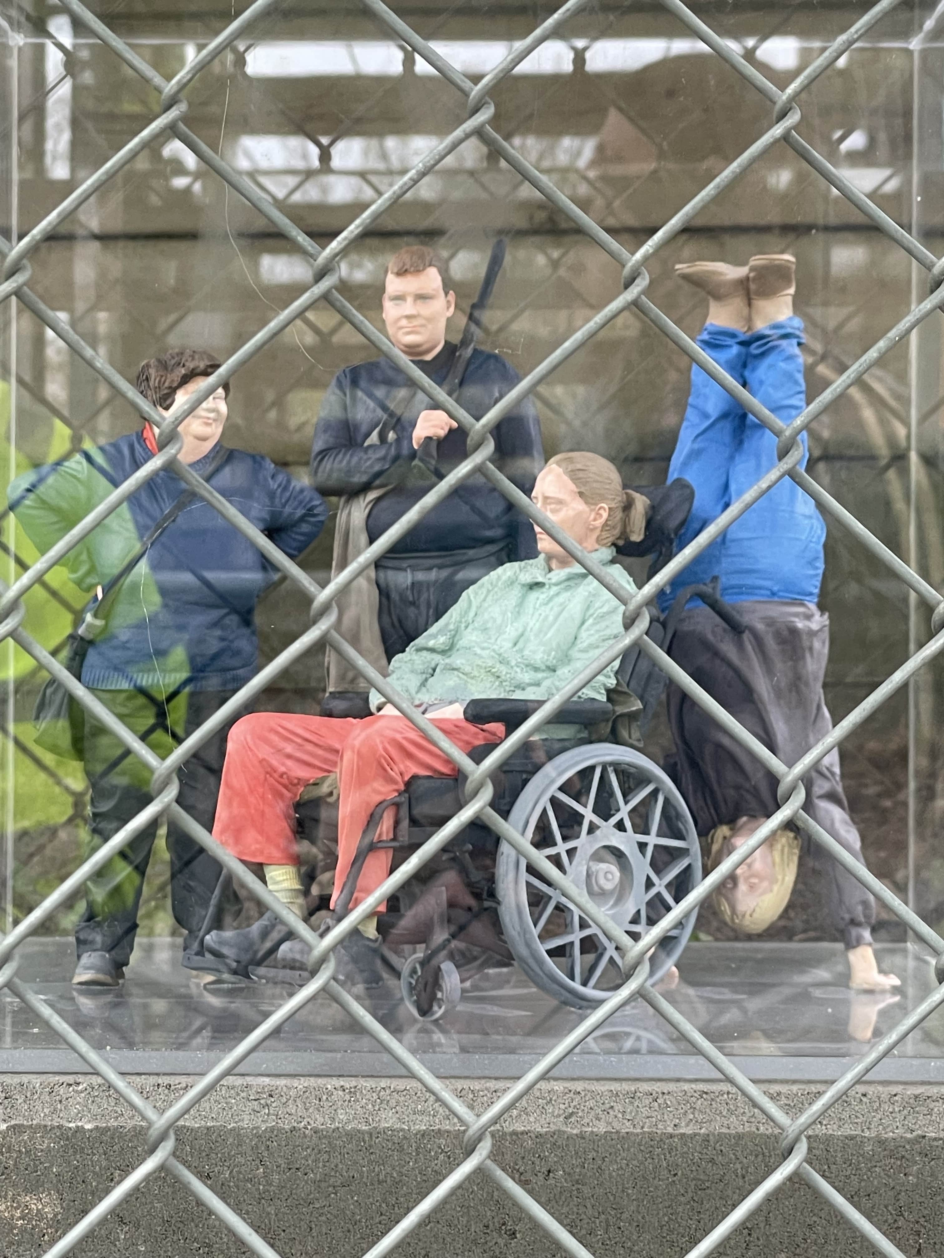 Ett konstverk bestående av fyra vaxdockor varav en sitter i rullstol och en står på huvudet.