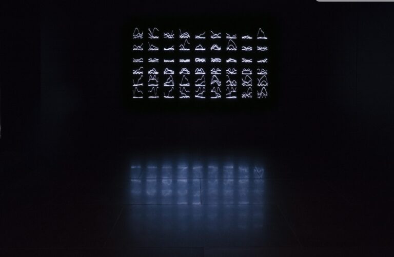A light installation consisting of small steel figures resembling runes, illuminated by LED lights in a dark room.