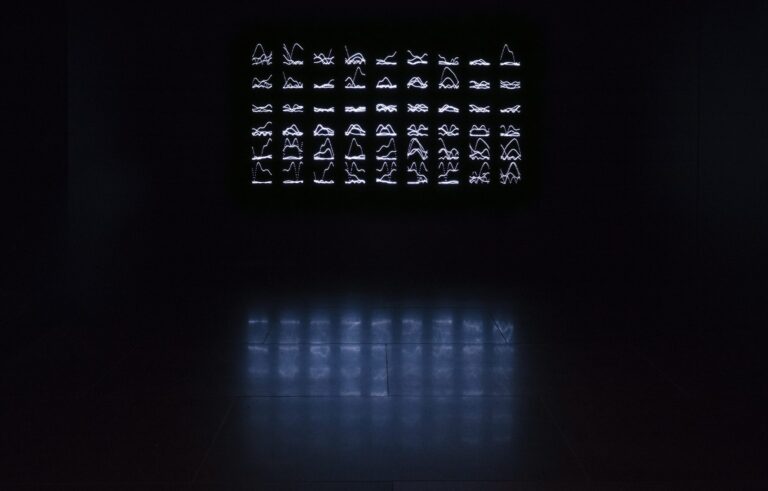 Ett ljusverk bestående av små figurer i stål som ser ut som runor, upplysta av LED-lampor i ett mörkt rum.
