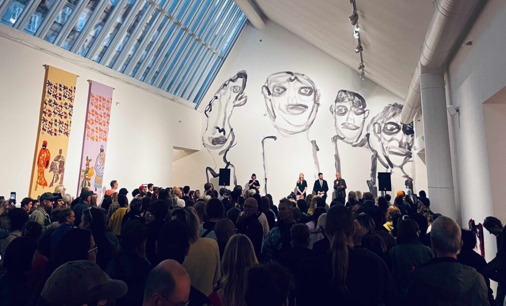 Kvällsfoto från konsthallens rum med en massa besökare och Alan Faulds verk med fyra streckgubbar som täcker hela bakre väggen i bakgrunden.