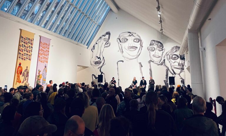 Kvällsfoto från konsthallens rum med en massa besökare och Alan Faulds verk med fyra streckgubbar som täcker hela bakre väggen i bakgrunden.