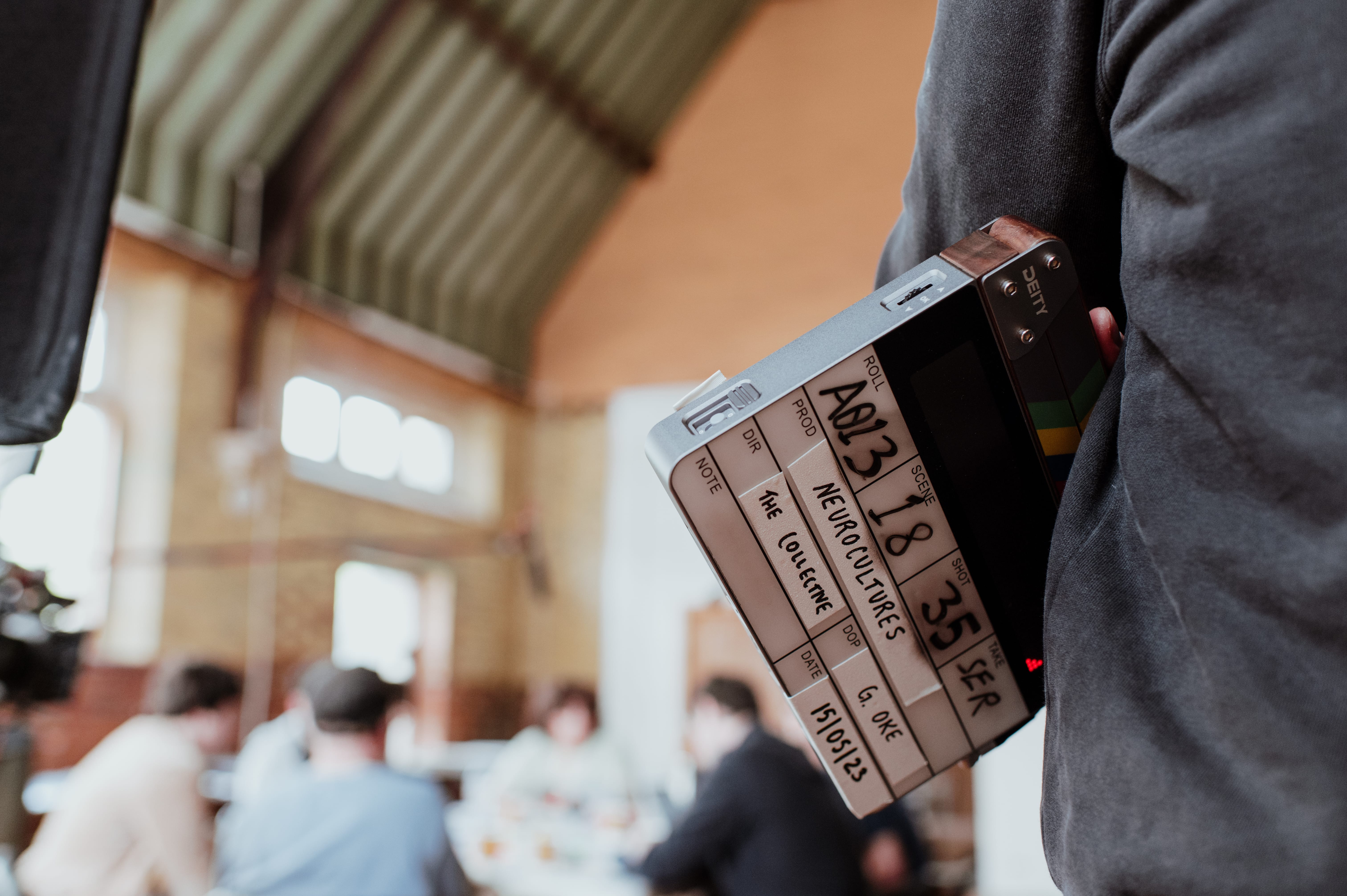 A hand holding a film clapperboard that says “Neurocultures.”