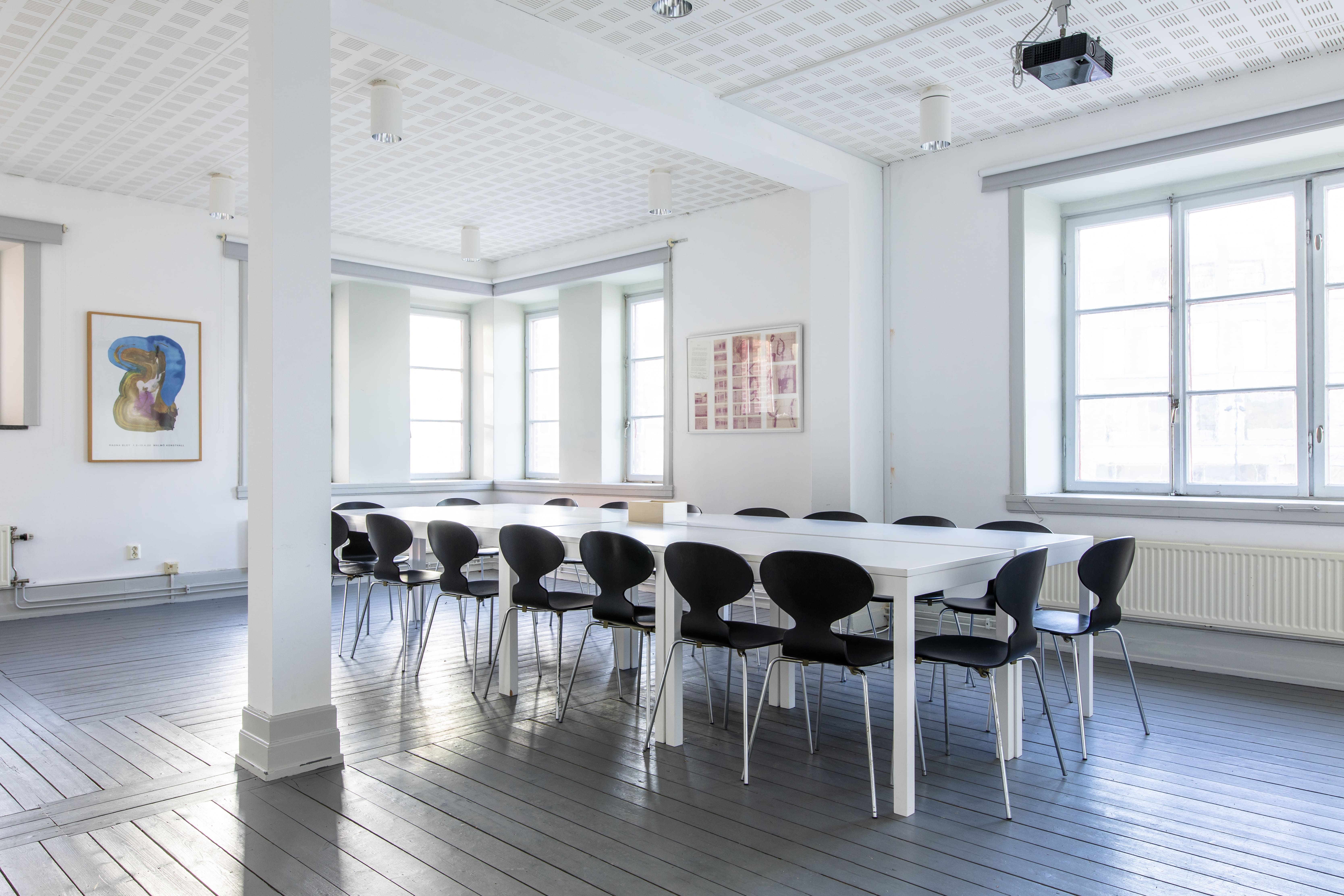 Mötesrum med tolv svarta stolar, vitt bord i ett ljust rum med några inramade posters på väggarna.