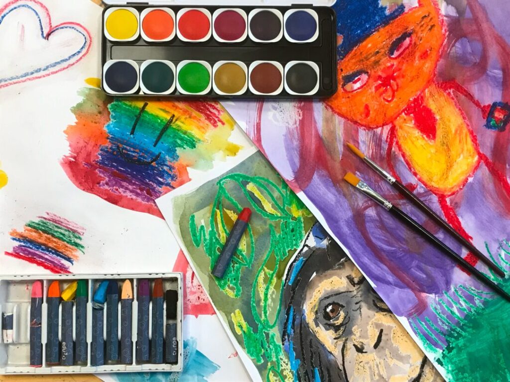 Färgglada kritor och färg tillsammans med målningar.