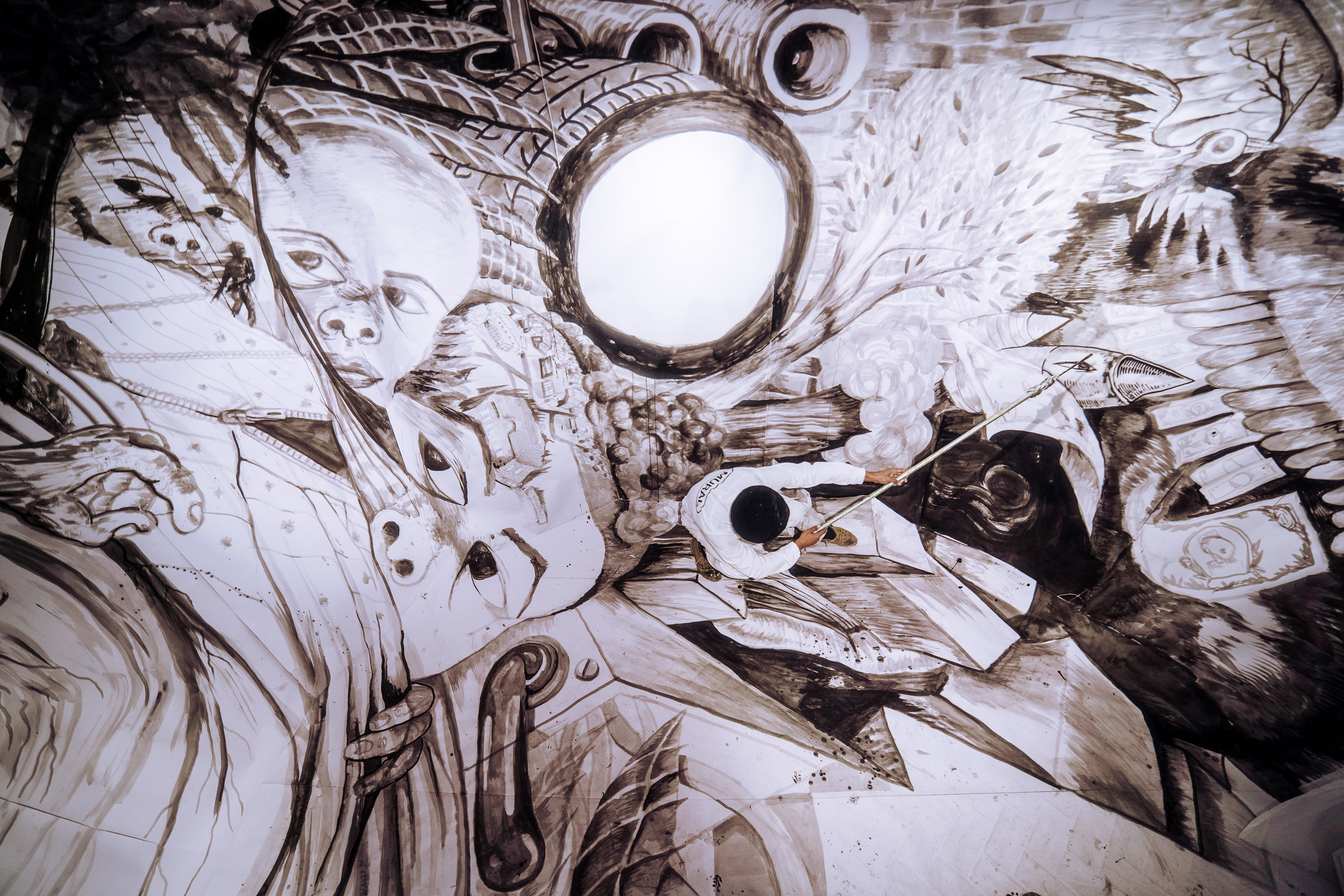 Konstnären Kim Demåne befinner sig mitt i sin egen muralmålning i full färd med att måla detaljer i en figur.