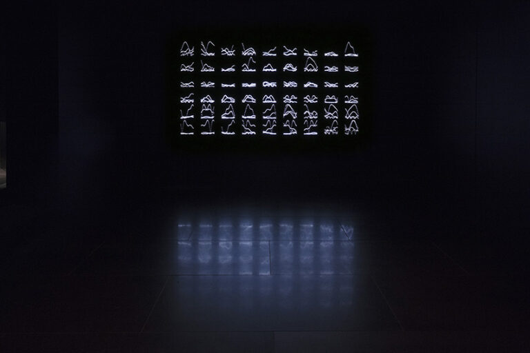 Ett ljusverk bestående av små figurer i stål som ser ut som runor, upplysta av LED-lampor i ett mörkt rum.