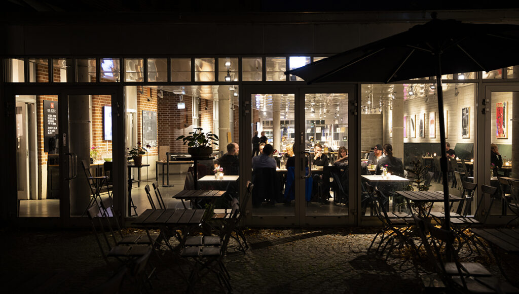 Restaurang Smak fotograferat från uteserveringen och in under en dunkel höstkväll. Ett sällskap sitter samlat i den varmt upplysta lokalen. Det ser gemytligt ut.