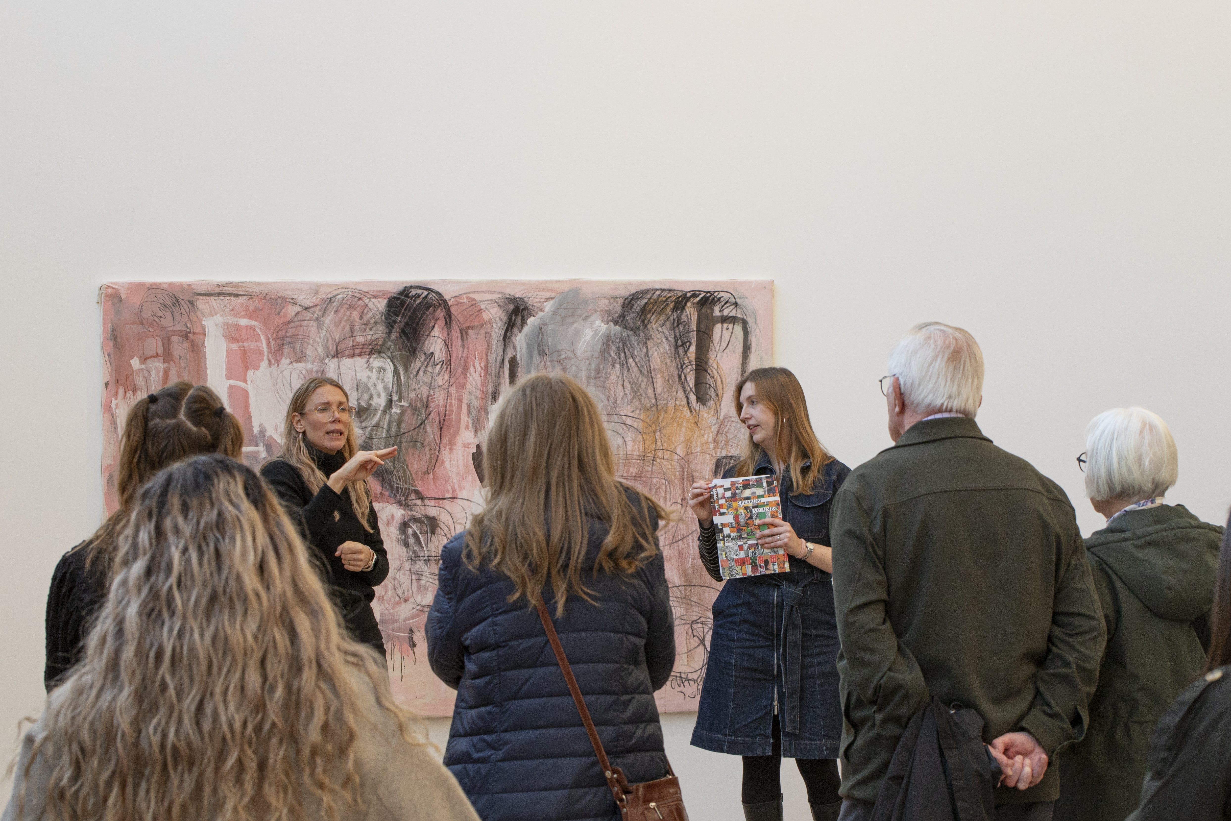 Visning med två guider som står framför ett stort rosa abstrakt verk och cirka 10 personer som står runtomkring och lyssnar.