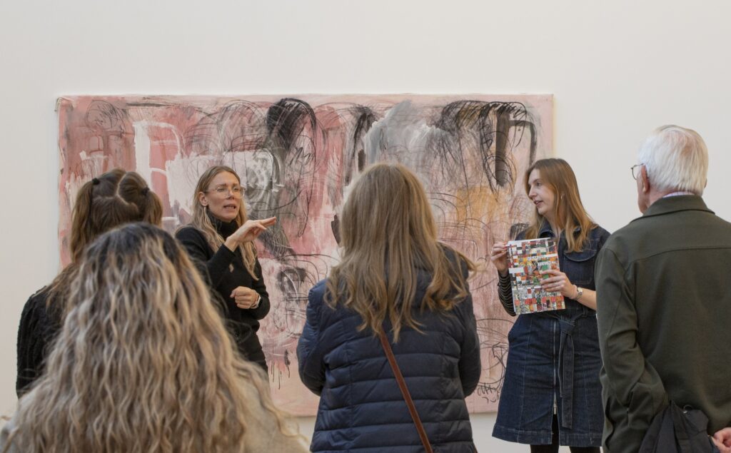 Guided tour with two guides standing in front of a large pink abstract artwork, with around 10 people gathered around listening.