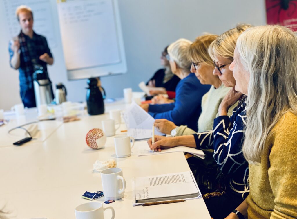 Äldre kvinnor sitter vid ett bord med texter och kaffekoppar framför sig och diskuterar litteratur.