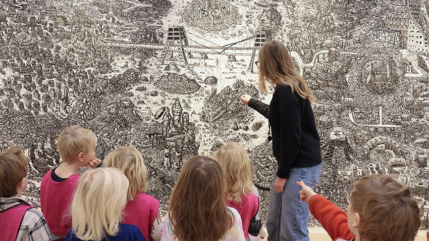 En av Malmö Konsthalls pedagoger visar detaljer i en stor teckning för en grupp barn.