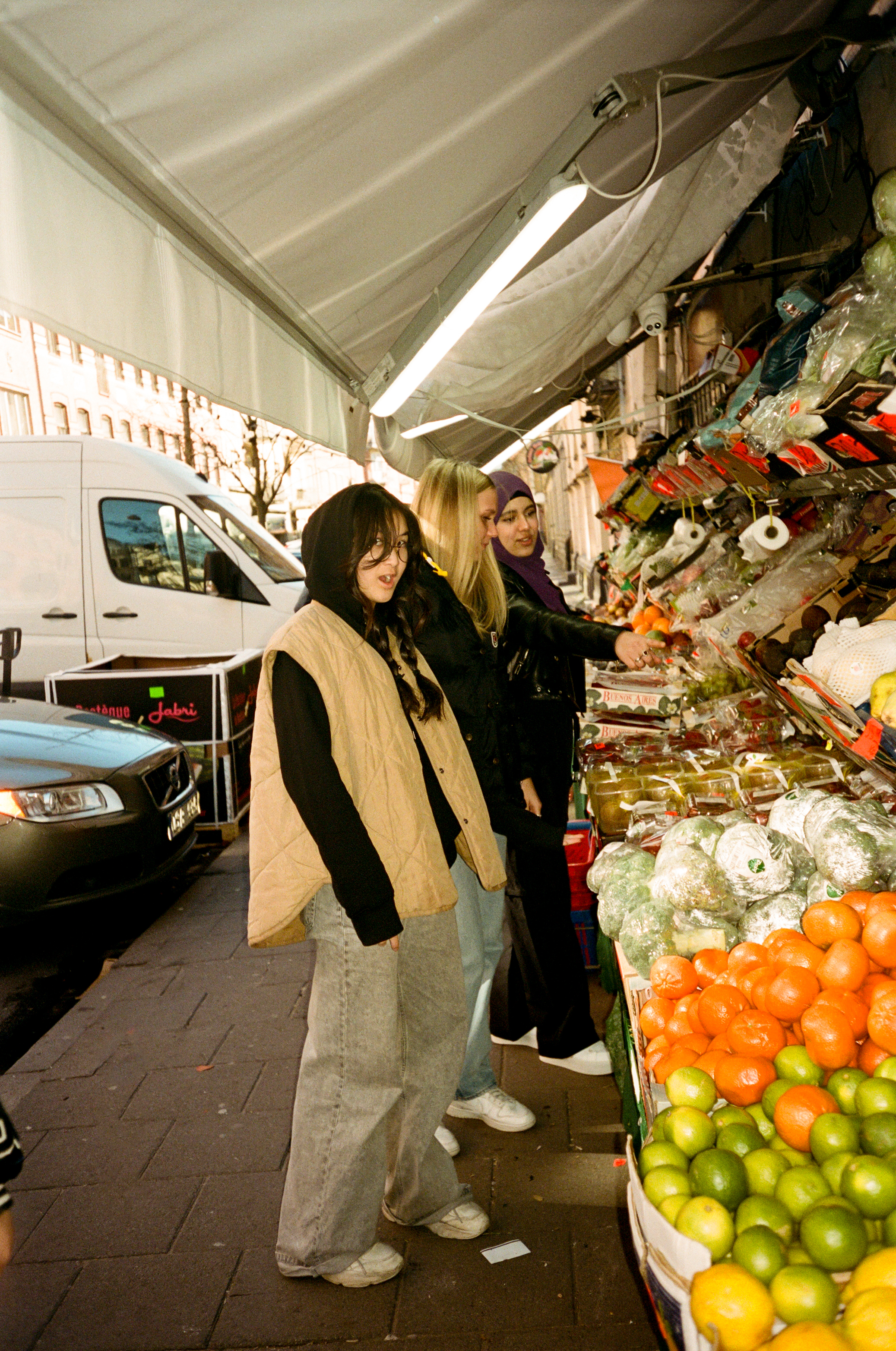 Tre tjejer står framför ett livs på möllan i Malmö. Det är apelsiner och lime i stora lådor utanför affären.
