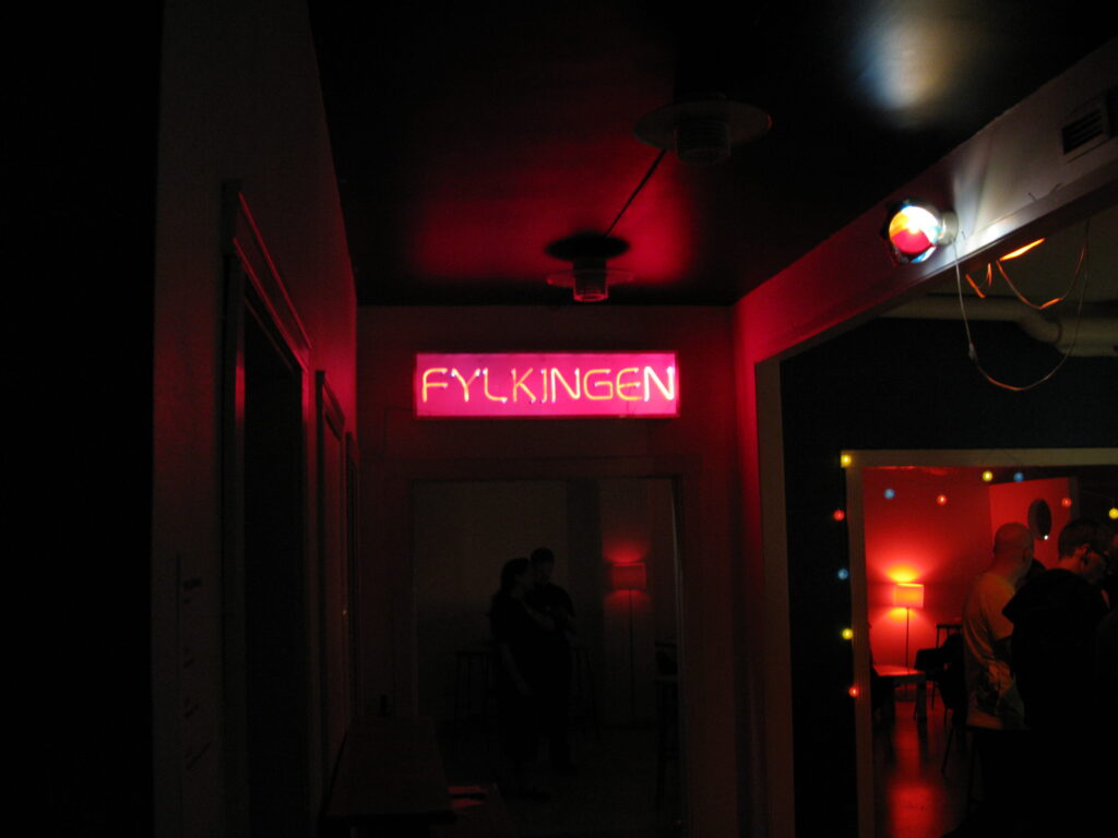 Ett mörkt rum med rött sken där texten Fylkiingen är upplyst på väggen.