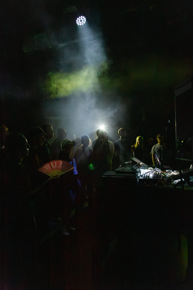 Ett mörkt, rökfyllt rum. En folkmassa står framför ett DJ-bås.