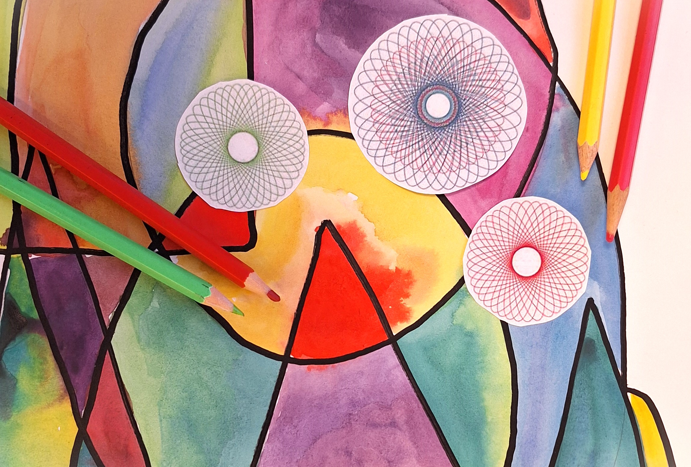 Färgglada pennor ligger på ett målat papper. På bilden ligger även tre utklippta spirografer i olika färger.