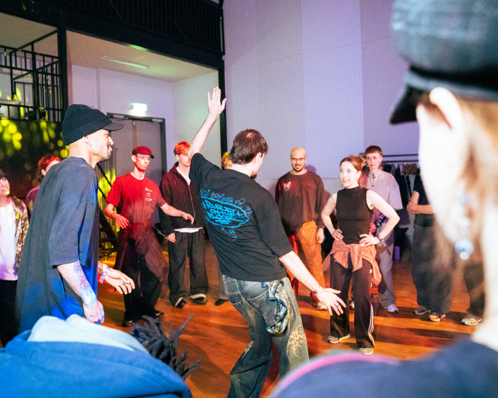Several people are dancing in a circle. The light is cool, blue and purple.